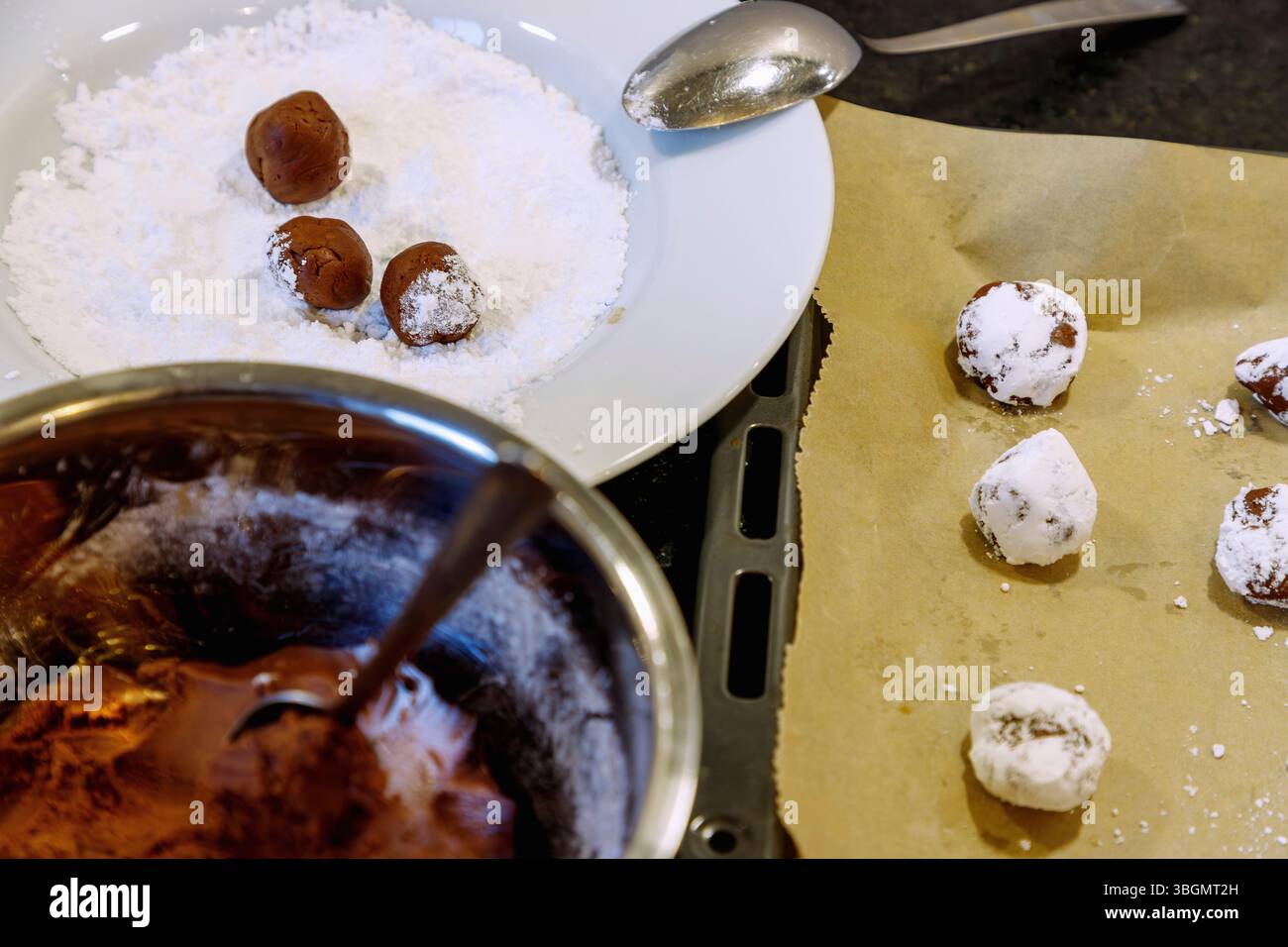 Chapeaux de neige pendant la préparation, pâte au chocolat formée en boules et roulée dans du sucre en poudre sur la plaque de cuisson avec du papier sulfurisé Banque D'Images