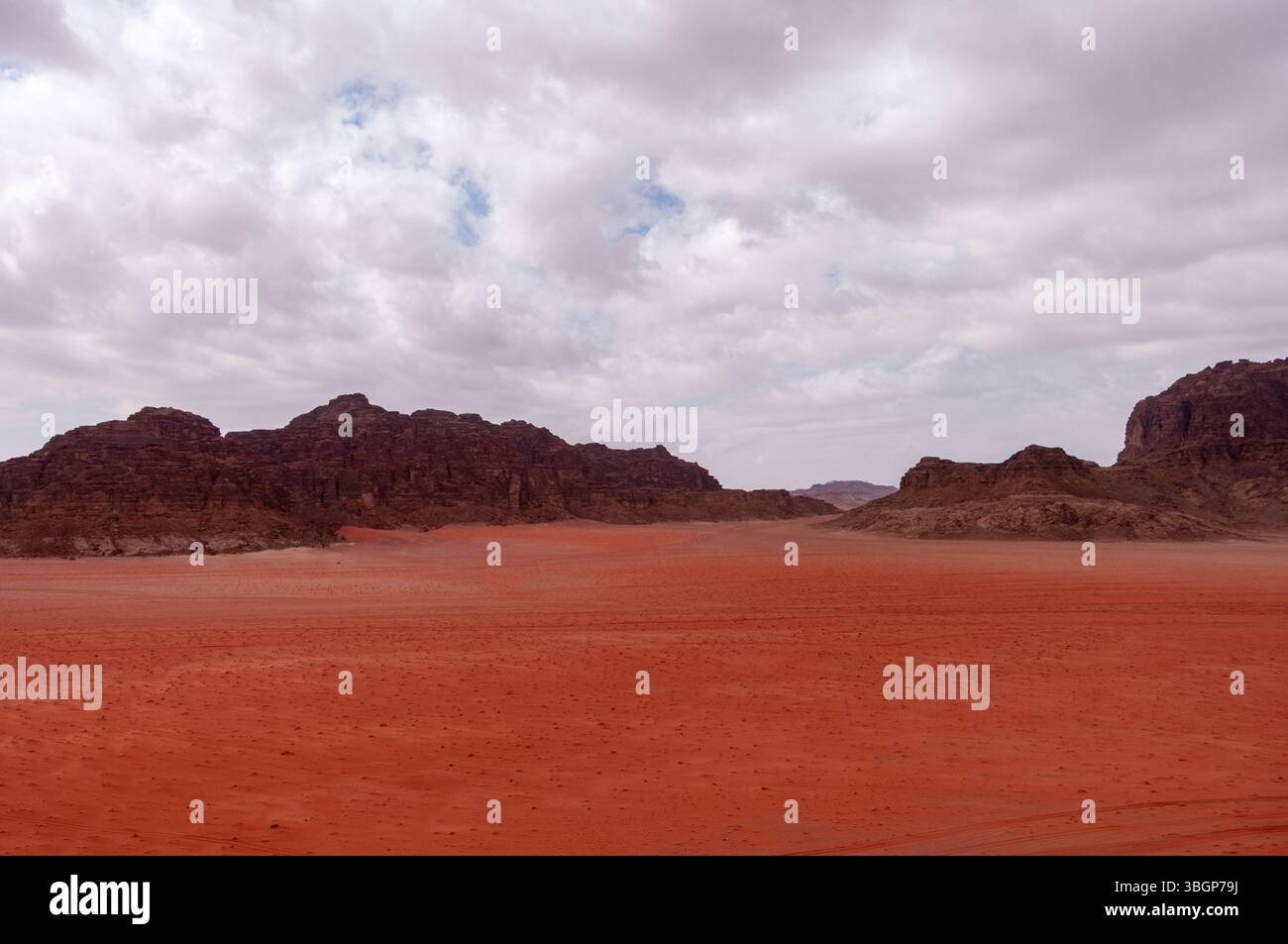 Un paysage désertique avec un ciel nuageux. Le ciel est principalement nuageux avec quelques taches de bleu. Le désert est aride et rocheux sans végétation Banque D'Images