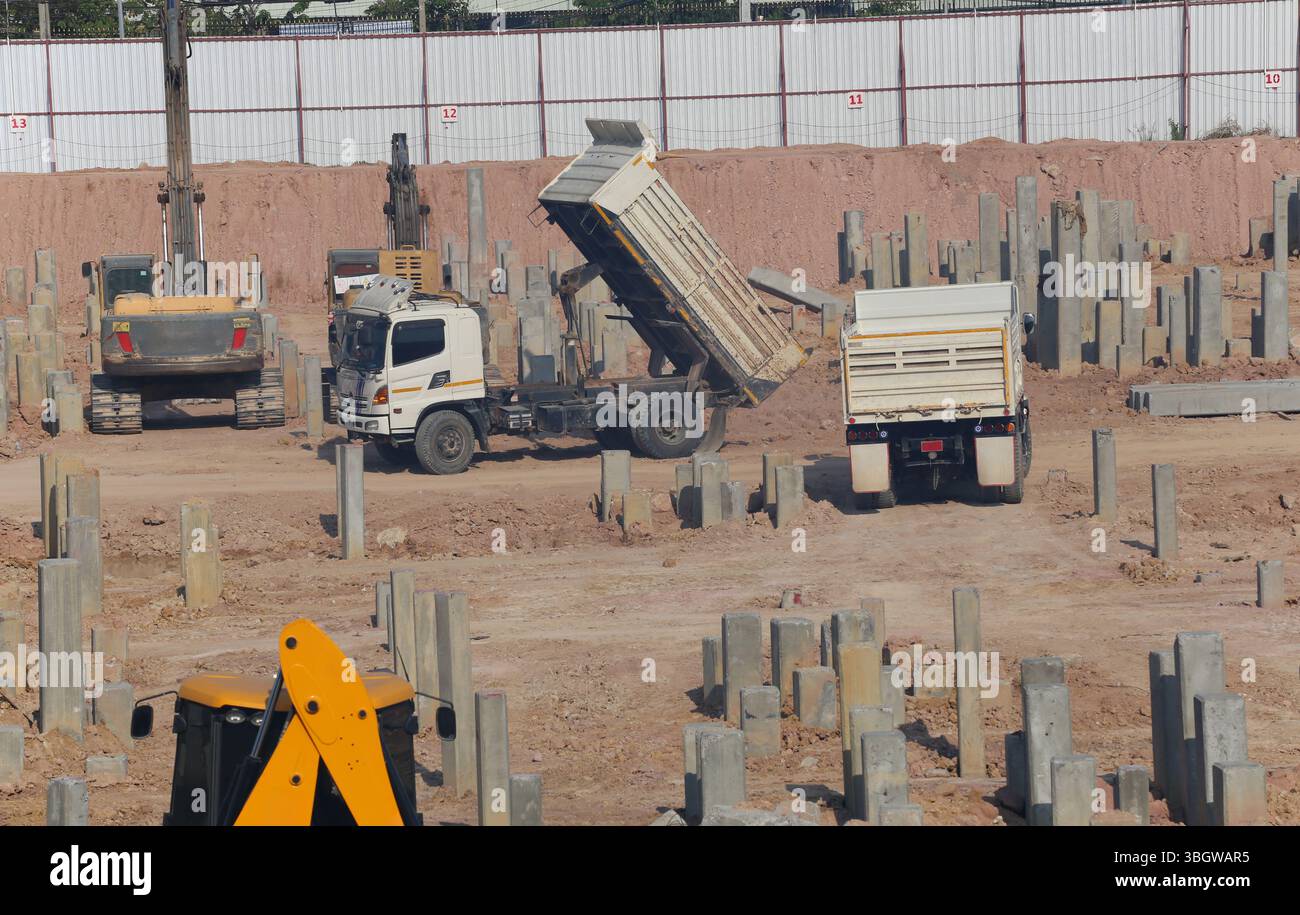Un chantier de construction animé avec des camions à benne basculante déchargeant des matériaux sur un terrain fraîchement excavé, symbolisant le développement actif des infrastructures Banque D'Images