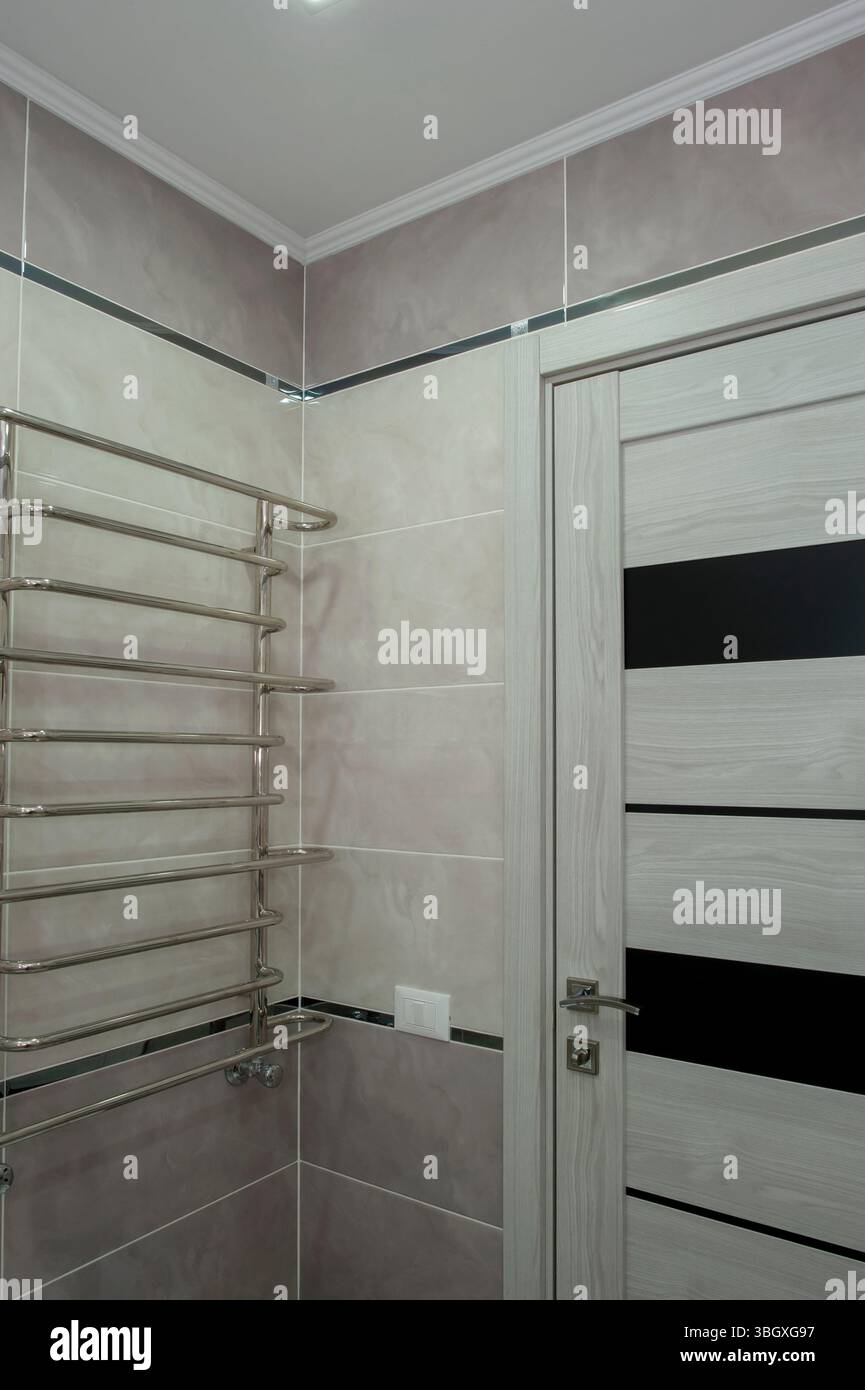 Grande salle de bains neuve lumineuse dans des couleurs claires avec carrelage gris chaud, porte blanche contre la chambre inachevée. Banque D'Images