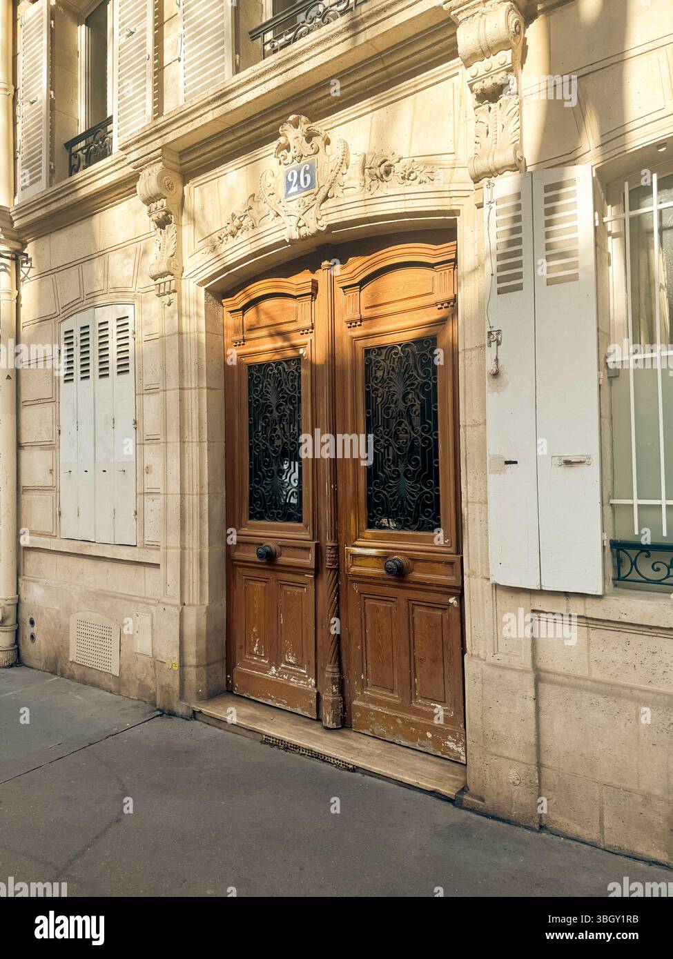 Une double porte en bois vieilli avec panneaux de verre et ferronnerie ornée sert d'entrée à un bâtiment parisien classique en pierre, avec le numéro Banque D'Images