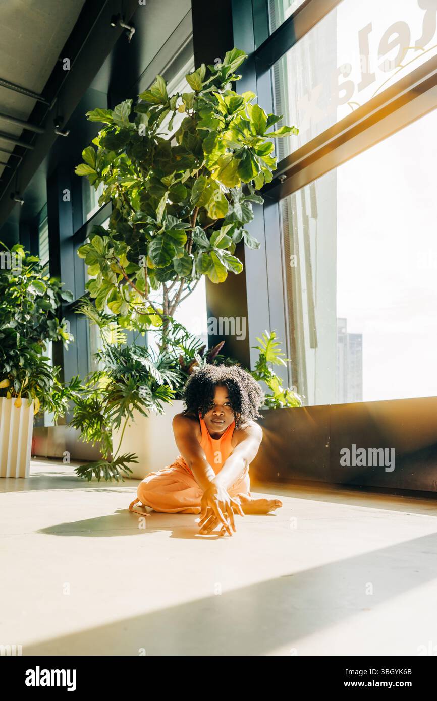 Femme assise en étirant les bras sur le sol intérieur ensoleillé Banque D'Images
