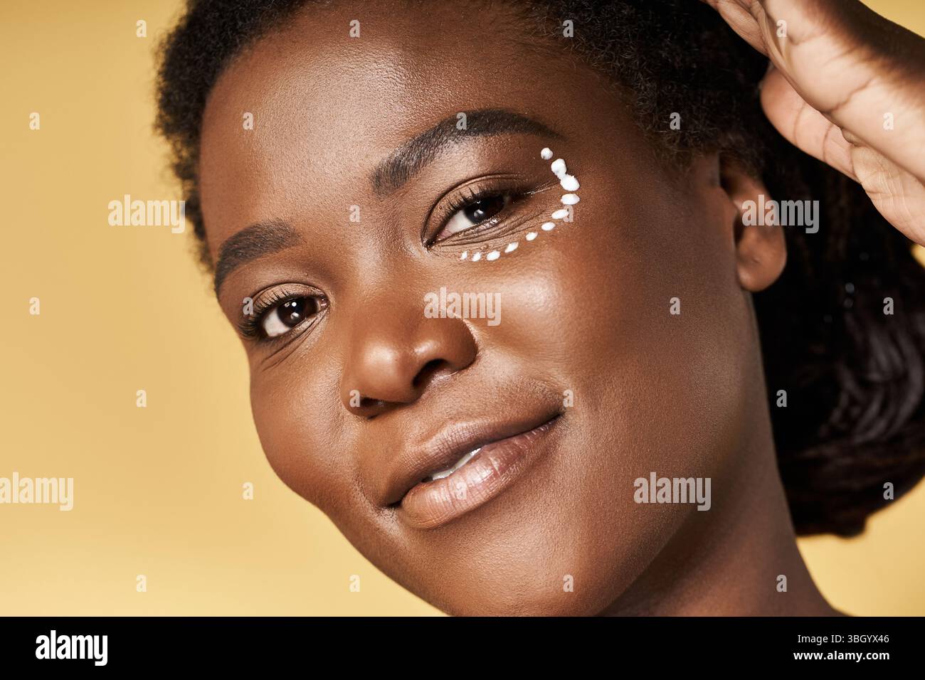 La peau rayonnante brille sur une jeune femme afro-américaine posant avec confiance dans un cadre de studio. Banque D'Images