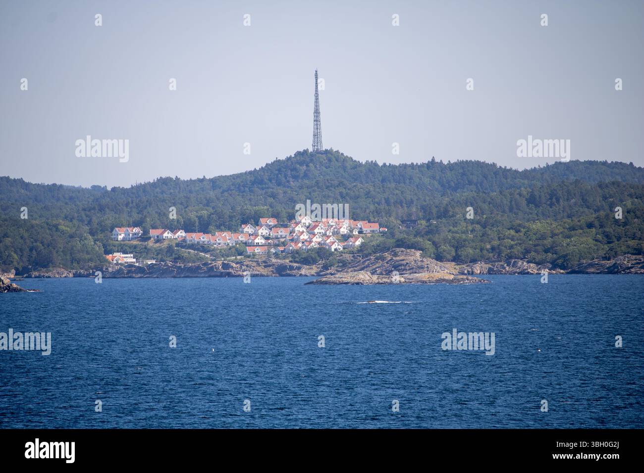 Norwegisches Küstenstädtchen mit Funkturm – Weiße Holzhäuser und bewaldete Hügel am Meer Banque D'Images