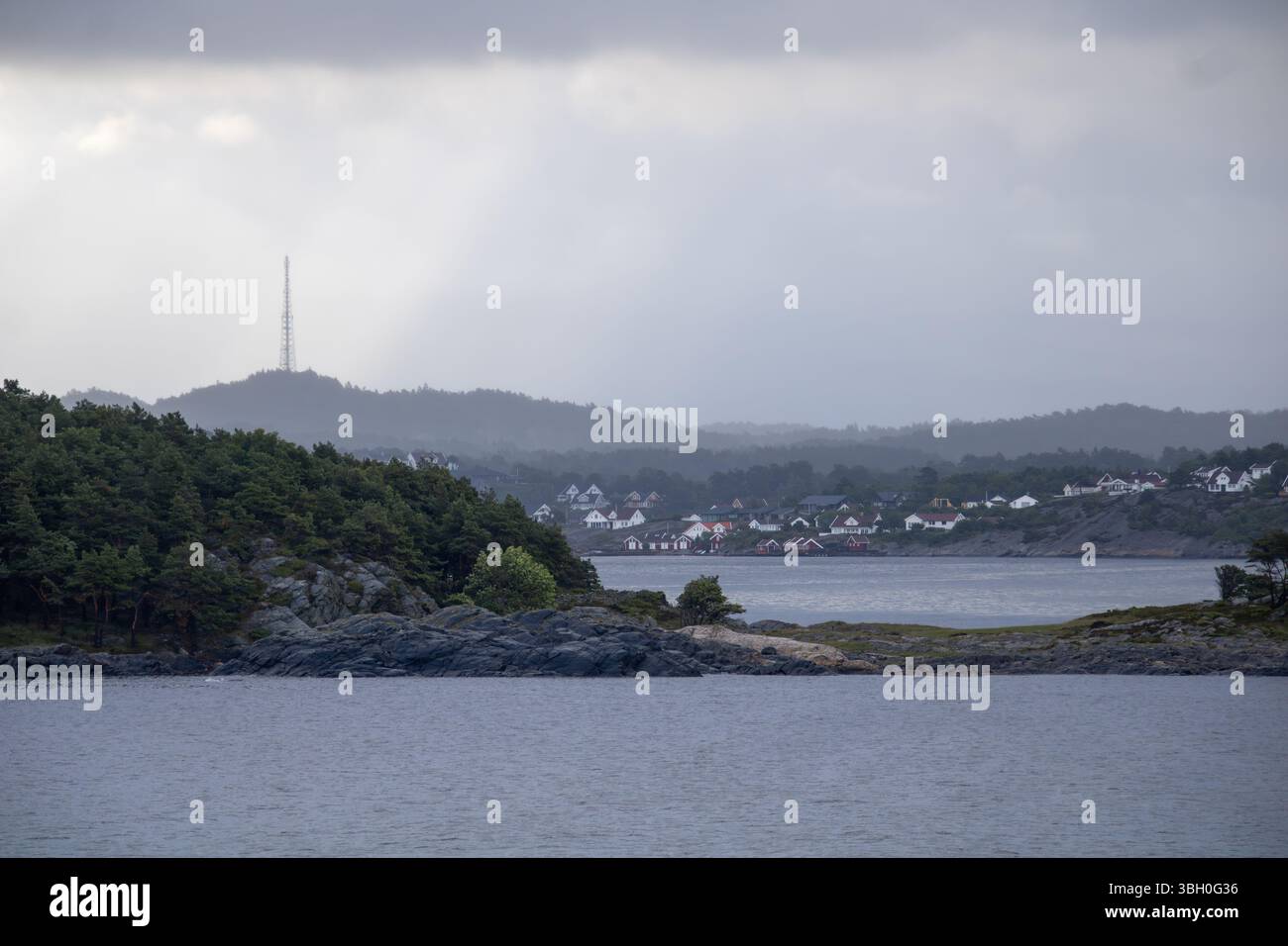 Norwegisches Küstenstädtchen mit Funkturm – Weiße Holzhäuser und bewaldete Hügel am Meer Banque D'Images