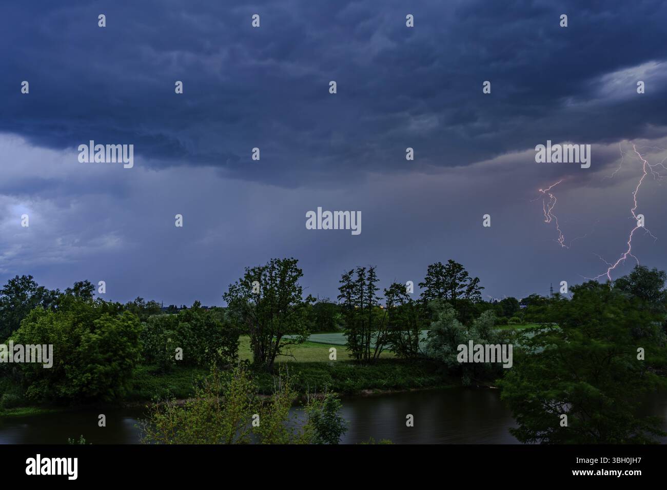 La foudre illumine un ciel sombre au-dessus des arbres et une rivière dans la nuit sombre, Bogen, basse-Bavière Banque D'Images