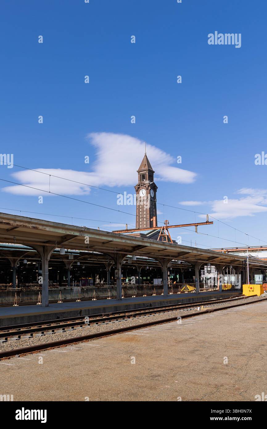 Vue sur l'emblématique tour de l'horloge du terminal de Hoboken depuis la passerelle au bord de la rivière, encadrée par un ciel dégagé et une architecture classique de la gare. Banque D'Images