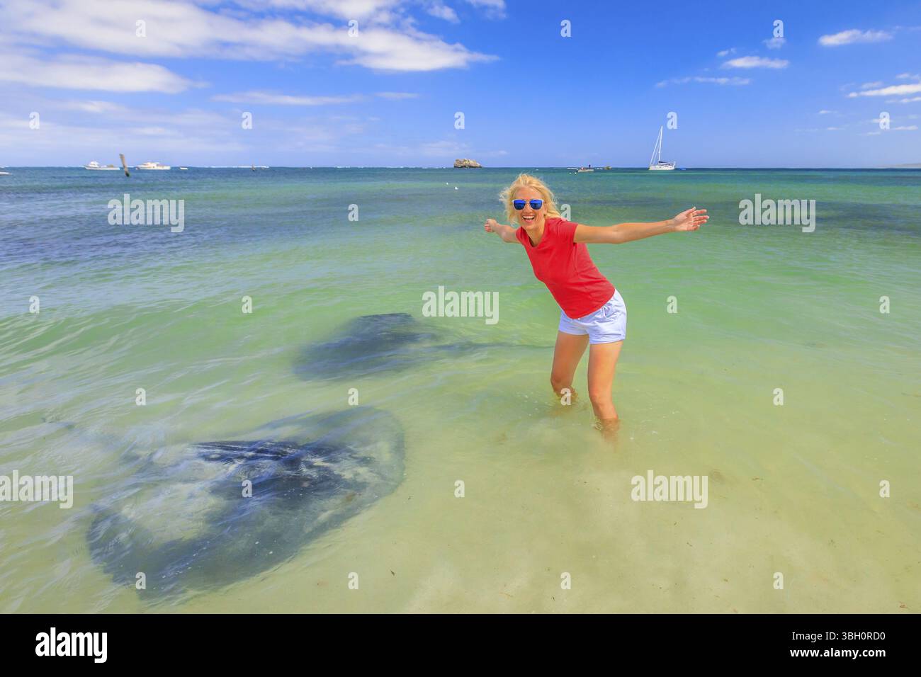Heureuse femme blonde à bras ouverts près de deux grands rayons australiens de l'aigle près de la rive dans Hamelin Bay, Australie occidentale. La touriste aime l'aigle stin Banque D'Images
