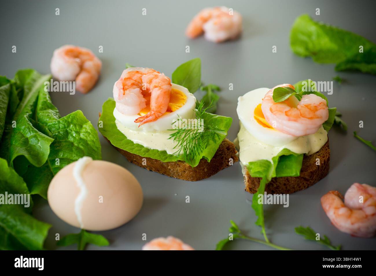 Sandwich avec oeuf, laitue et crevettes isolé sur fond gris. Banque D'Images