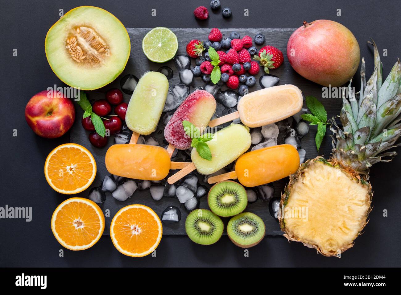Au centre sur des glaçons une variété de cônes de sorbet de fruits autour des ingrédients fruits et baies sur un fond noir. Variété de cônes de sorbet de fruits et baies. Horizontal. Vue de dessus. Banque D'Images
