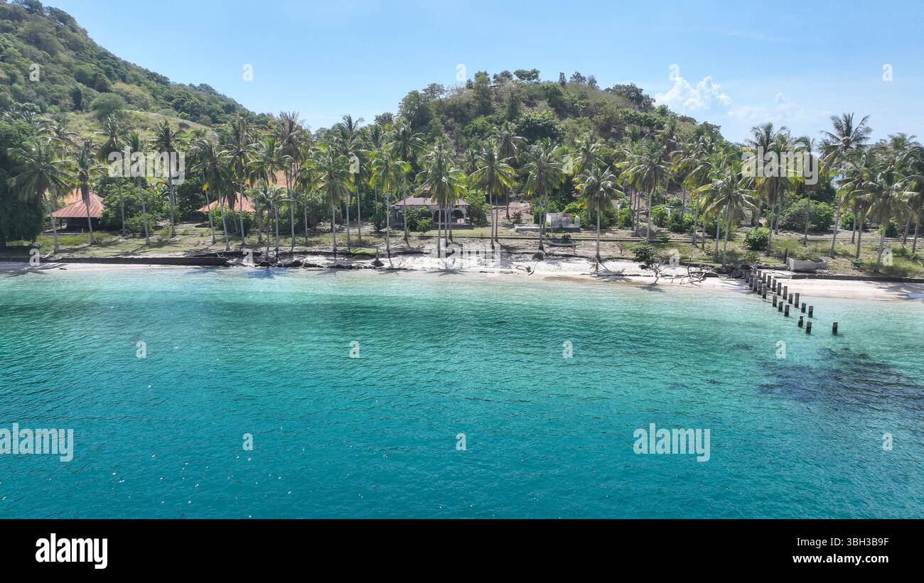 Les palmiers bordent un littoral paisible avec une eau cristalline et des cottages rustiques nichés au pied d'une colline verdoyante, offrant un tropical serein Banque D'Images