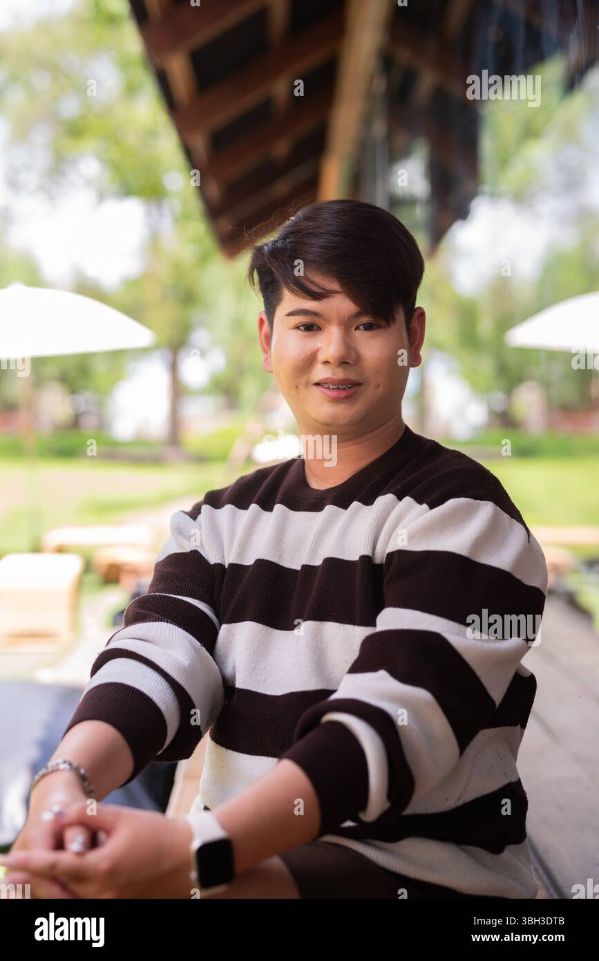 Jeune homme gay mignon assis à l'extérieur dans le restaurant café pendant la journée Banque D'Images