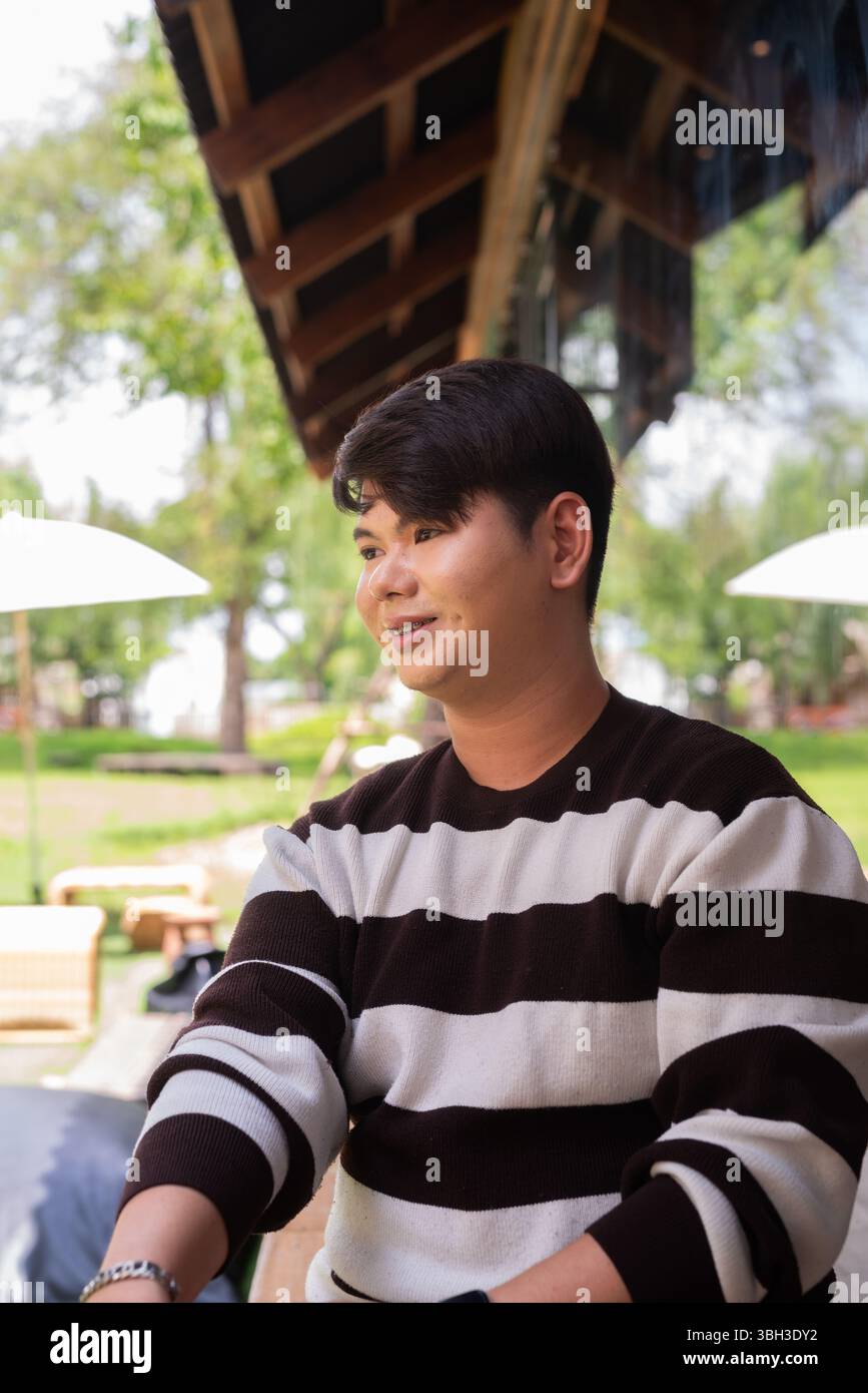 Jeune homme gay mignon assis à l'extérieur dans le restaurant café pendant la journée Banque D'Images