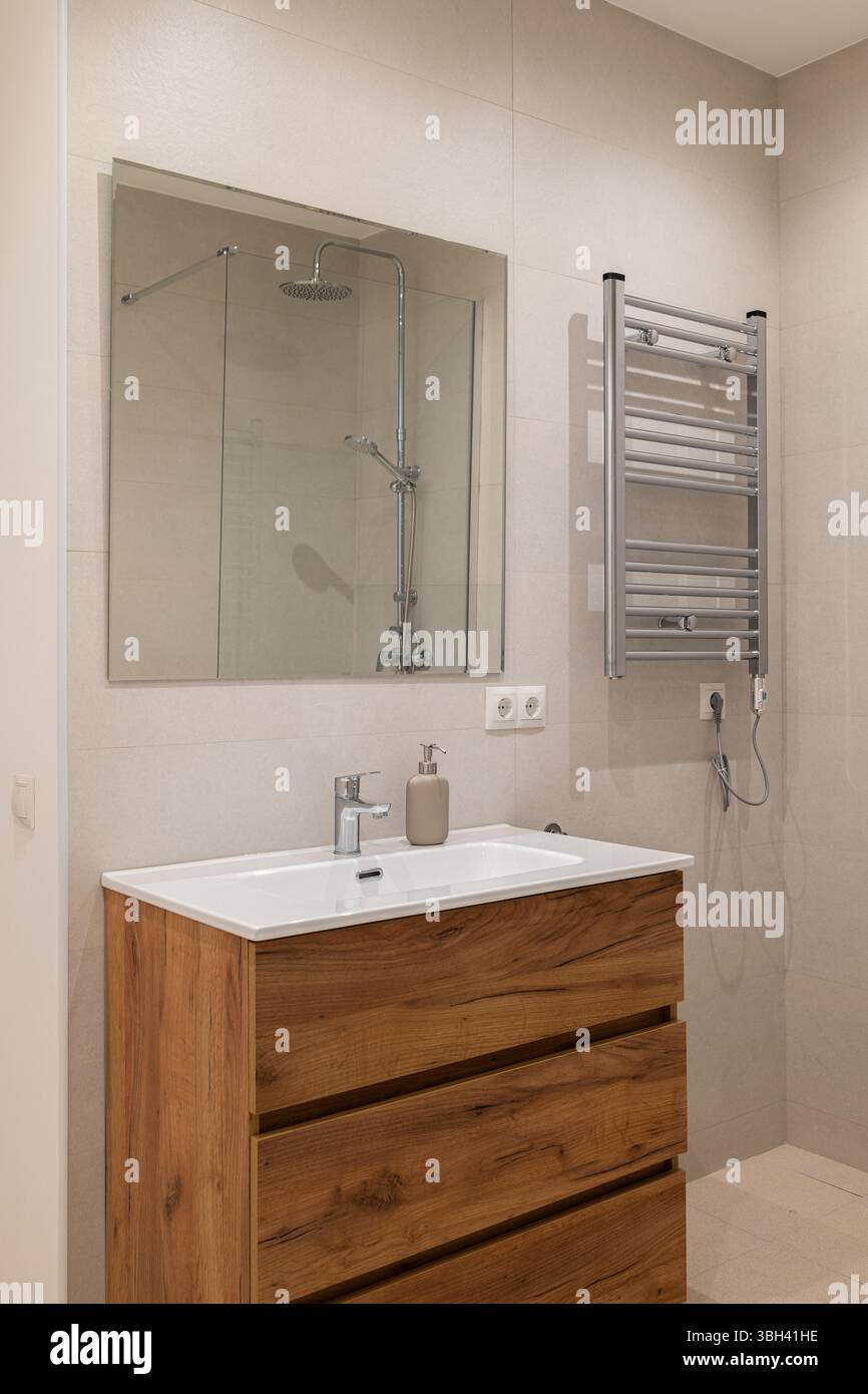 Gros plan de la vanité de salle de bains avec tiroirs en bois, évier en céramique blanche et robinet chromé sous miroir Banque D'Images