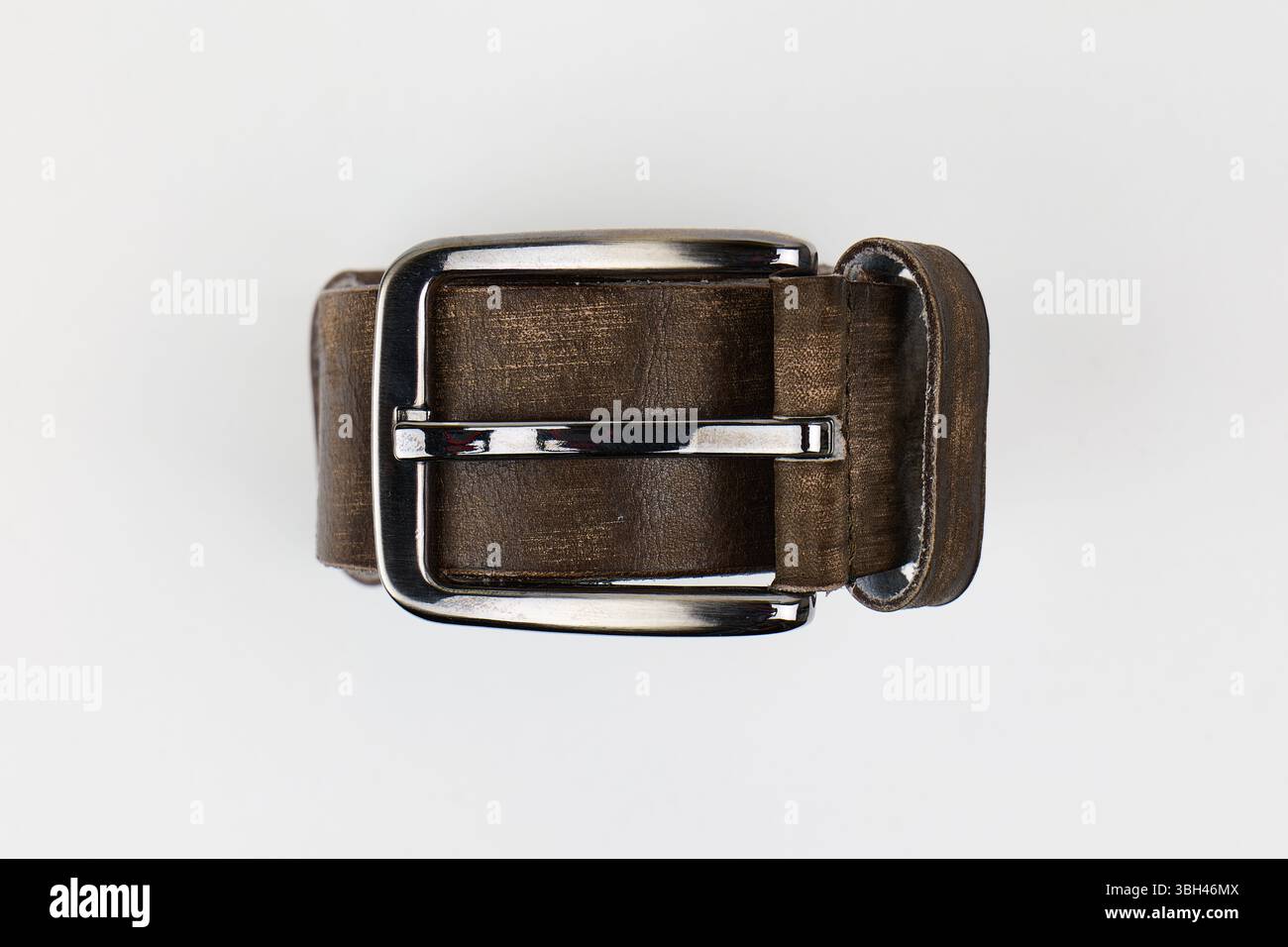 Une ceinture en cuir marron avec une boucle argentée brillante placée sur un fond blanc. Photo de haute qualité Banque D'Images