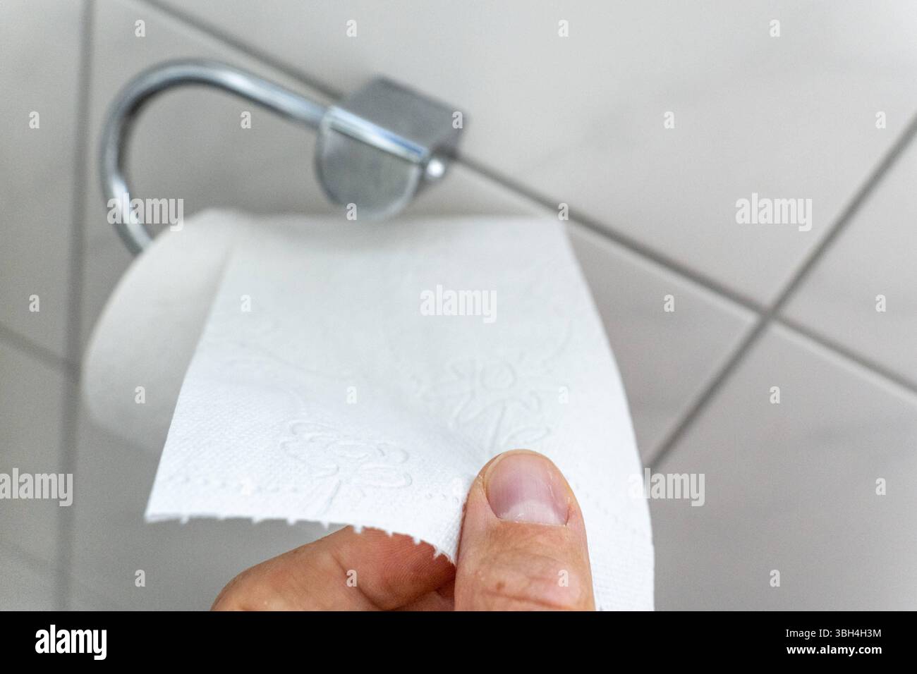 Bavière, Allemagne - 24 mai 2025 : une main tend pour le papier toilette sur le support dans la salle de bain - un moment quotidien dans le ménage qui représente visuellement le sujet de l'hygiène, de la fonctionnalité et des exigences sanitaires. *** Eine hand greift nach Toilettenpapier an der Halterung im Badezimmer ein alltäglicher moment im Haushalt, der das Thema Hygiene, Funktionalität und Sanitärbedarf visuell darstellt. Banque D'Images