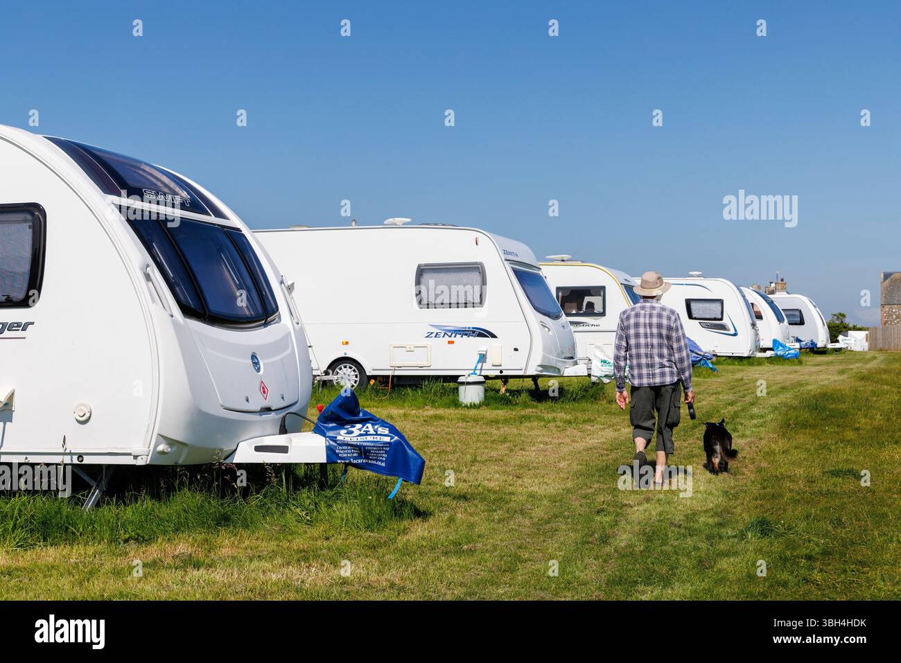 Homme promenant le chien devant la rangée de caravanes entreposées, Pembrokeshire, pays de Galles, Royaume-Uni Banque D'Images