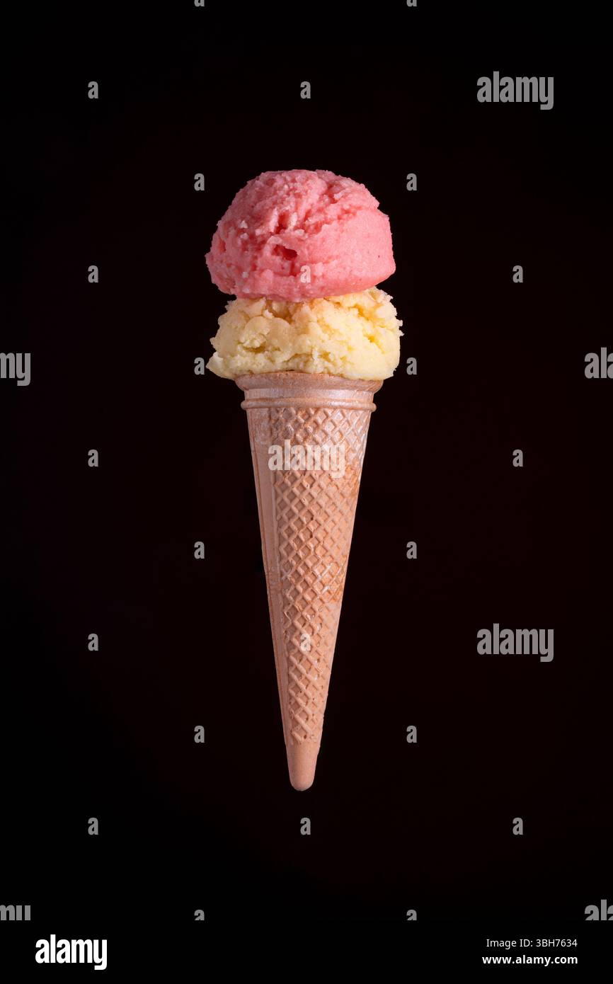Photo studio d'un cornet de crème glacée double scoop aux saveurs de fraise et de vanille, isolé sur un fond noir dramatique. Parfait pour me dessert Banque D'Images