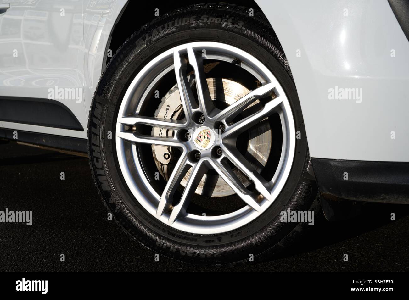 Un pneu de voiture avec un logo de la marque Michelin dessus. Le pneu est noir et argenté. La voiture est garée sur une route mouillée Banque D'Images
