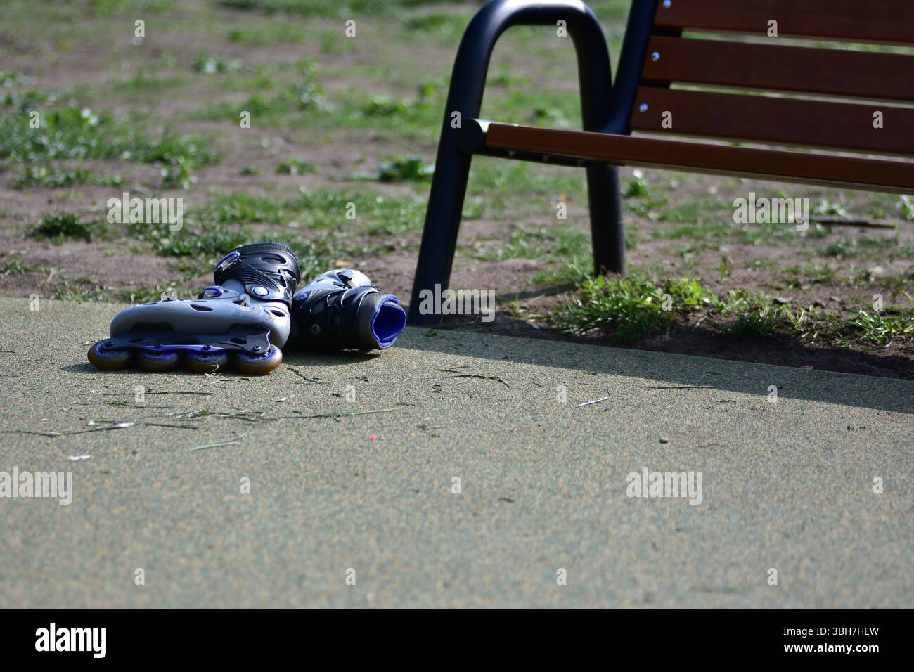 Une paire de lames de rouleau laissées à côté d'un banc dans une aire de jeux par une journée ensoleillée. L'image capture un moment paisible après le temps de jeu, symbolisant le repos, le Banque D'Images