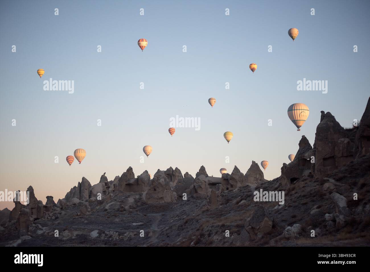 Les montgolfières colorées flottent gracieusement au-dessus des cheminées de fées distinctives de la Cappadoce, éclairées par la douce lumière de l'aube. Banque D'Images