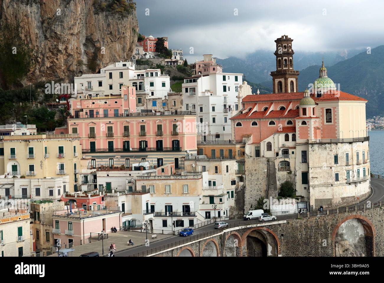 Une falaise spectaculaire et un ciel tonnerre se dessinent au-dessus des bâtiments aux couleurs pastel de l'église Atrani & Maria Santa Maddalena. Côte amalfitaine, Italie Banque D'Images