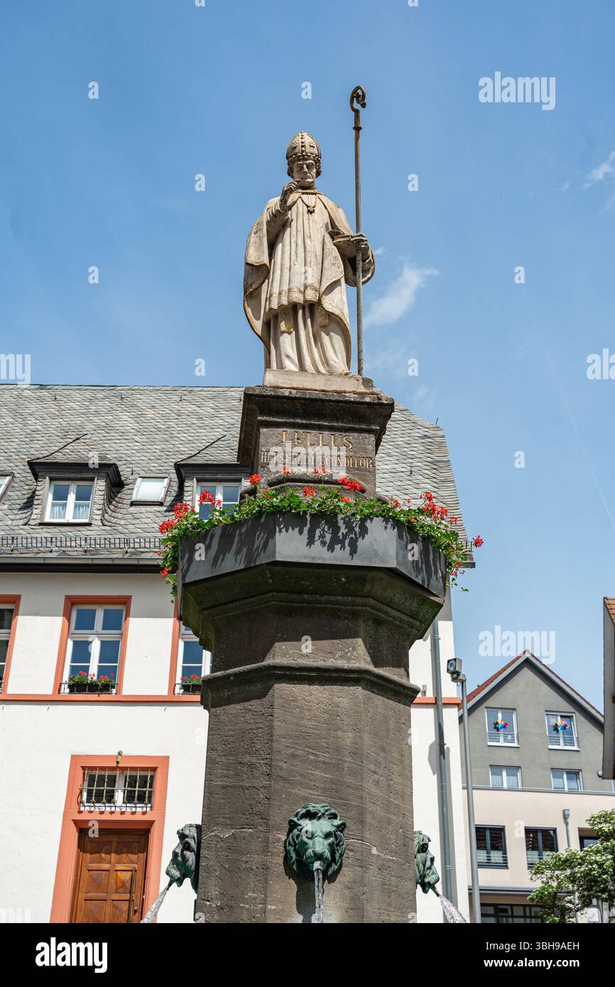 Statue en pierre d'un personnage religieux debout au sommet d'une fontaine, posée contre un ciel bleu clair. La sculpture détaillée représente une figure tenant un bâton Banque D'Images