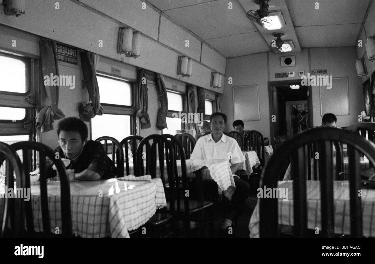 Les passagers dînent et se reposent dans une voiture-restaurant de train chinoise au milieu de nappes à carreaux et d'un décor classique - une scène intemporelle du voyage en train dans la Chine des années 2000 Banque D'Images