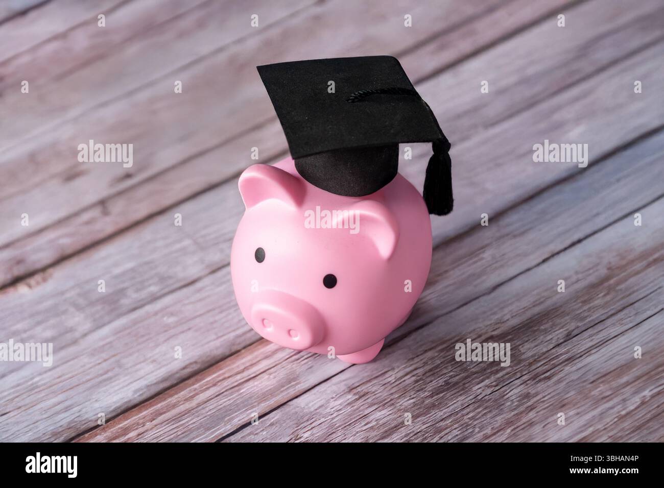 Une tirelire rose et une casquette de graduation sur une table en bois. Concept d'éducation, d'épargne ou d'objectifs futurs. Banque D'Images