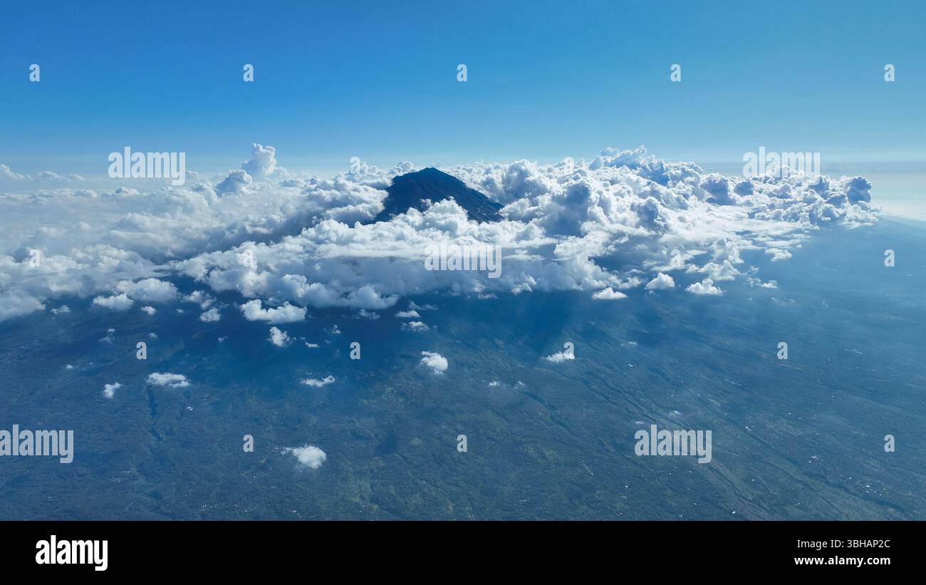 Les nuages tourbillonnent autour du pic volcanique, révélant les pentes escarpées et les riches forêts verdoyantes. La scène capture la beauté sauvage de cette île tropicale Banque D'Images