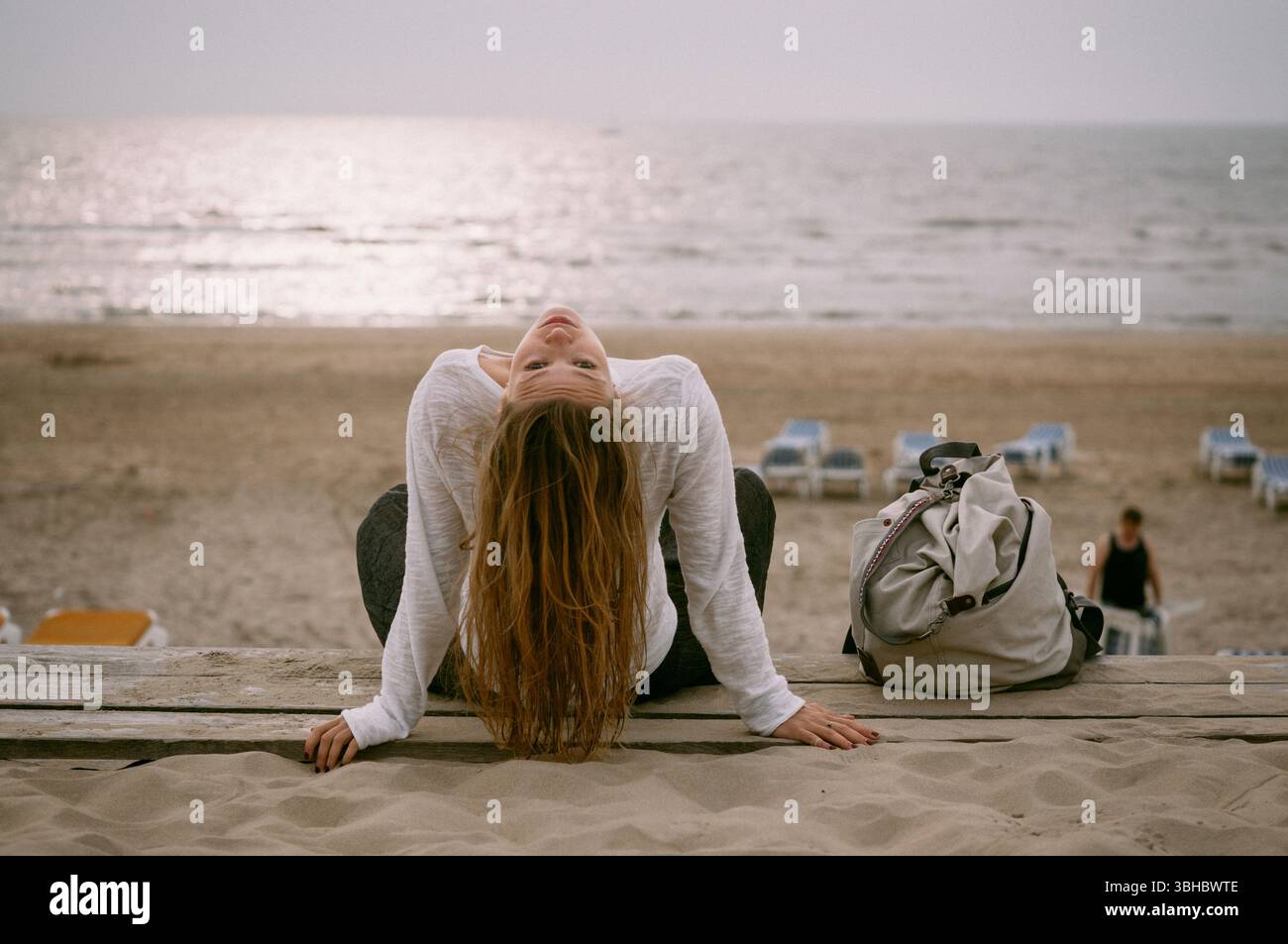 Femme penchée en arrière sur le banc de plage, face au coucher du soleil avec une ambiance calme Banque D'Images