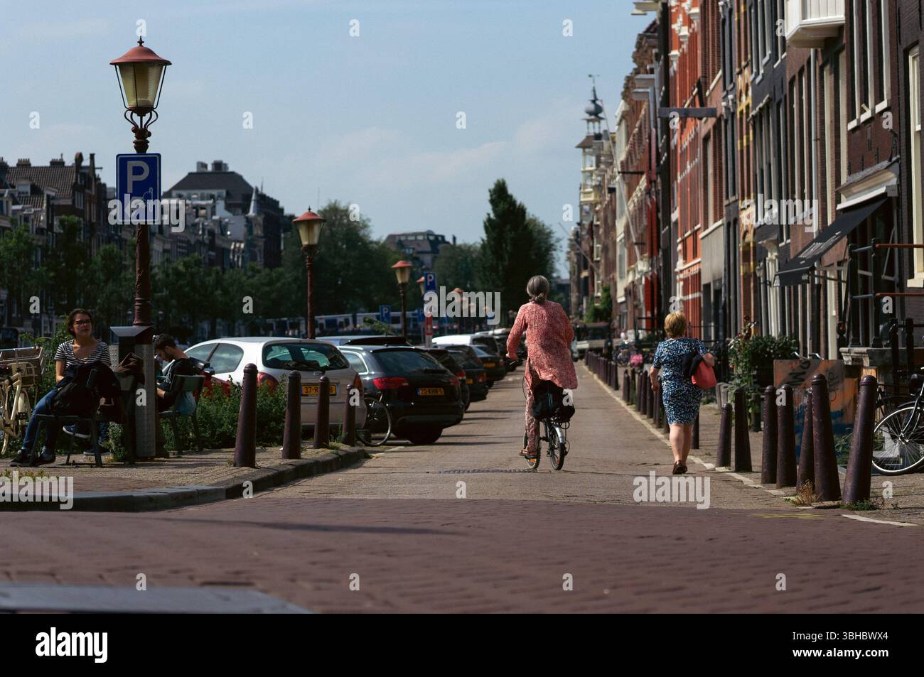 Cycliste et piétons sur une rue ensoleillée d'Amsterdam par le canal Banque D'Images