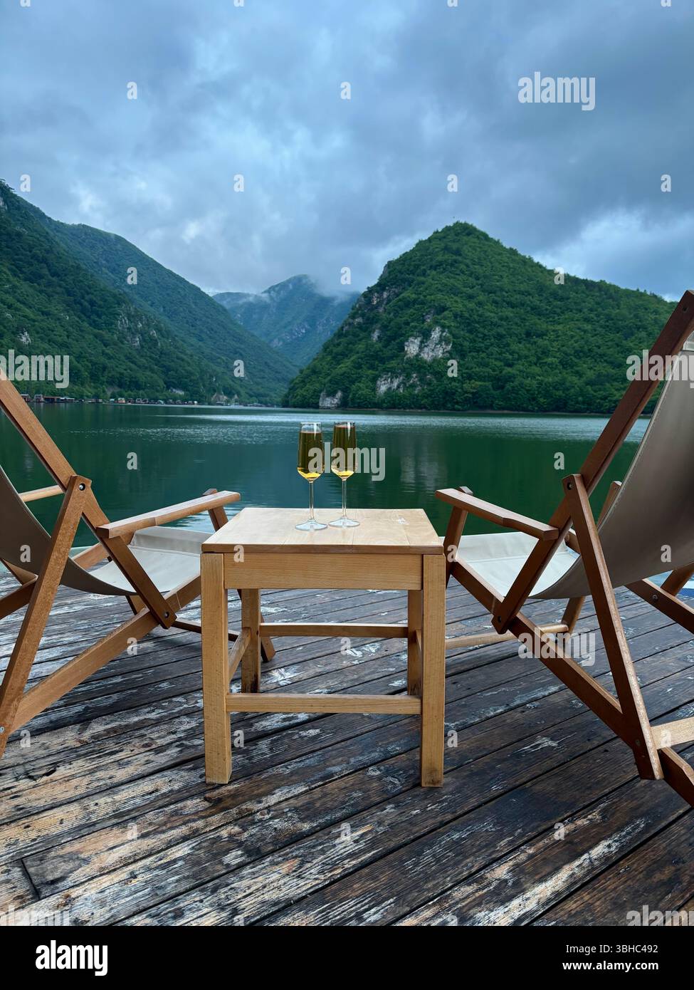 Deux chaises longues et verres de vin mousseux surplombant un lac alpin paisible par une journée d'été ensoleillée. Banque D'Images