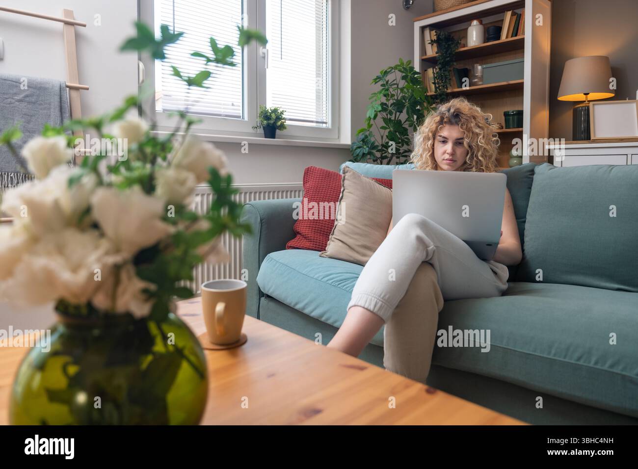 Jeune femme travaillant à distance de l'intérieur confortable de la maison, tapant sur ordinateur portable tout en étant assis confortablement sur le canapé, équilibrant la productivité, la concentration, la créativité, un Banque D'Images