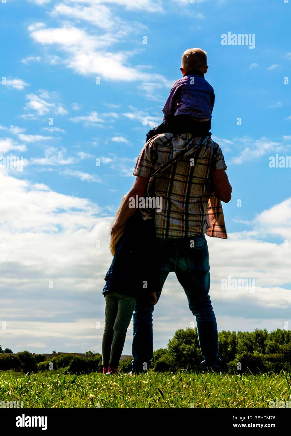 Un père se tient dos à la caméra, tenant un enfant sur ses épaules et un autre à ses côtés. Tous les trois regardent le ciel, qui est Banque D'Images