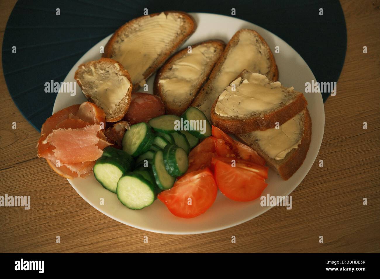 Une assiette de petit-déjeuner traditionnelle d'Europe de l'est faite maison avec tranches de pain de seigle beurré, concombre frais, tomates et saucisses séchées. Banque D'Images