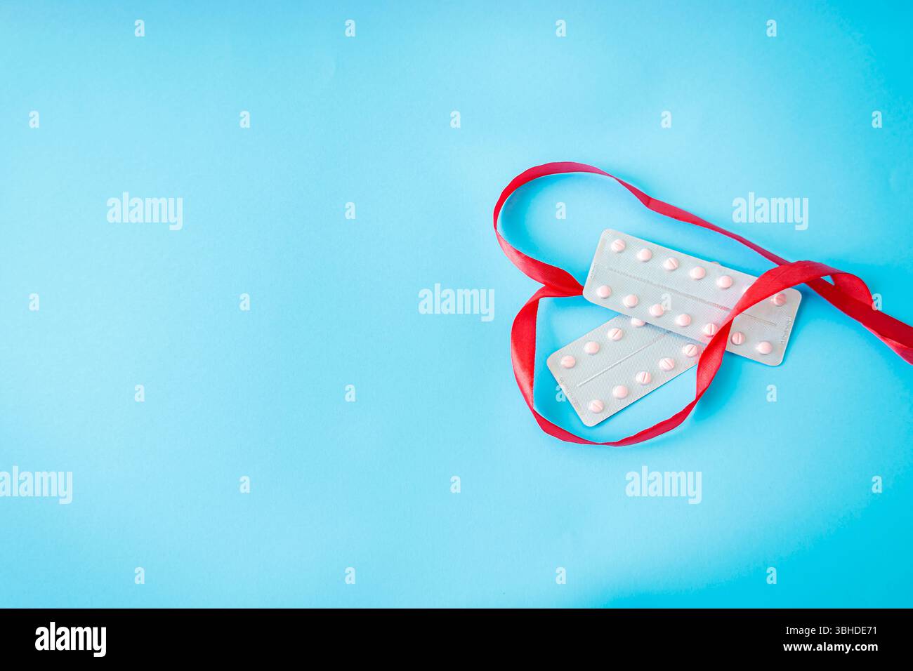 Pilules contraceptives et ruban rouge en forme de coeur sur fond bleu pastel. Plan conceptuel sur la contraception, l'amour et les ri reproductifs Banque D'Images