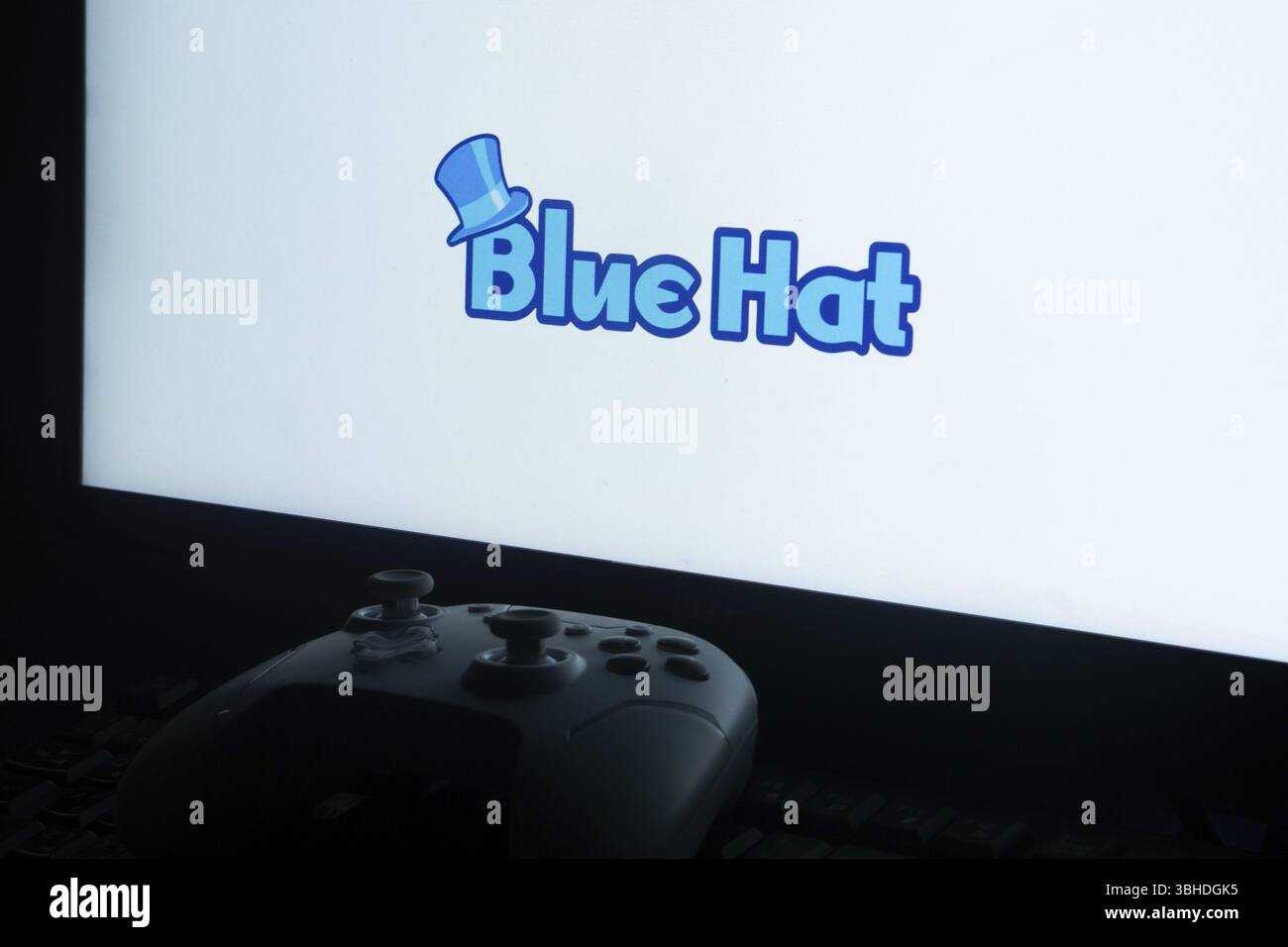 Logo Blue Hat à l'écran avec une manette de jeu vidéo au premier plan Banque D'Images