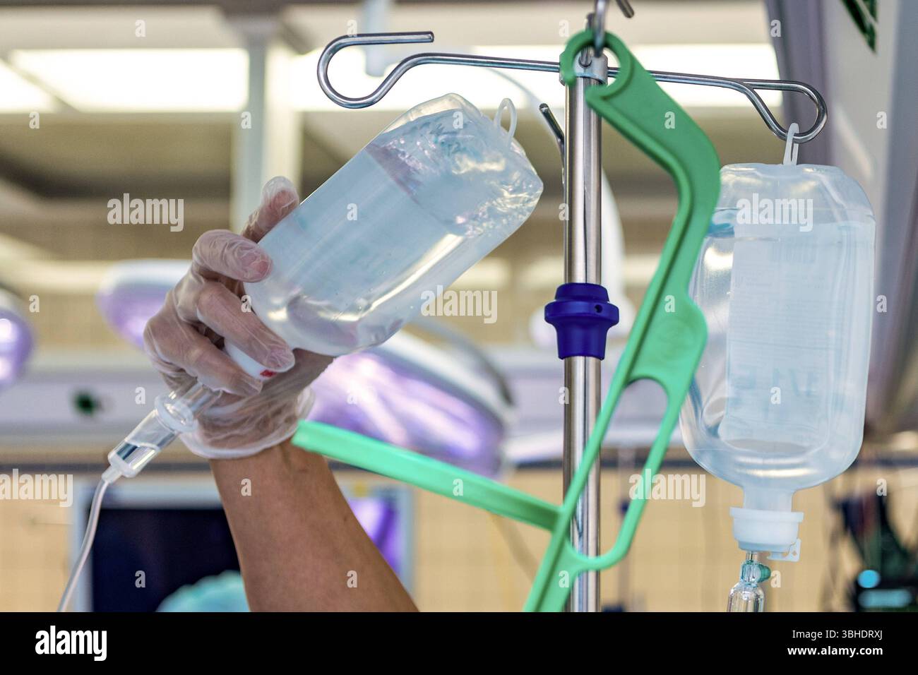 LK Osnabrück, Deutschland 30. Januar 2023 : Im Bild : dieses Bild zeigt eine hand einer medizinischen Fachkraft, die einen transparenten Einweghandschuh trägt und einen Infusionsbeutel mit einer klaren Flüssigkeit hält. Der Infusionsbeutel wird gerade an einem Infusionsständer befestigt oder davon abgenommen, was eine wichtige phase der Patientenversorgung im Krankenhaus darstellt. Ein zweiter Infusionsbeutel hängt bereits sicher am Ständer, was auf eine kontinuierliche Flüssigkeitszufuhr oder Medikamentenverabreichung hinweist. IM Hintergrund sind unscharfe medizinische Lampen mit ihrem charakt Banque D'Images