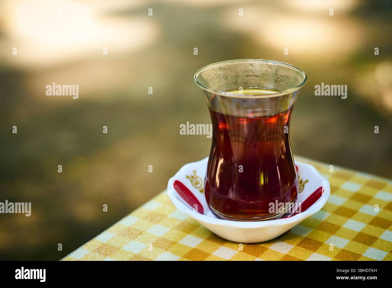 Un gros plan de thé noir aromatique dans un verre armudu classique, placé sur une nappe à carreaux brillante. Banque D'Images