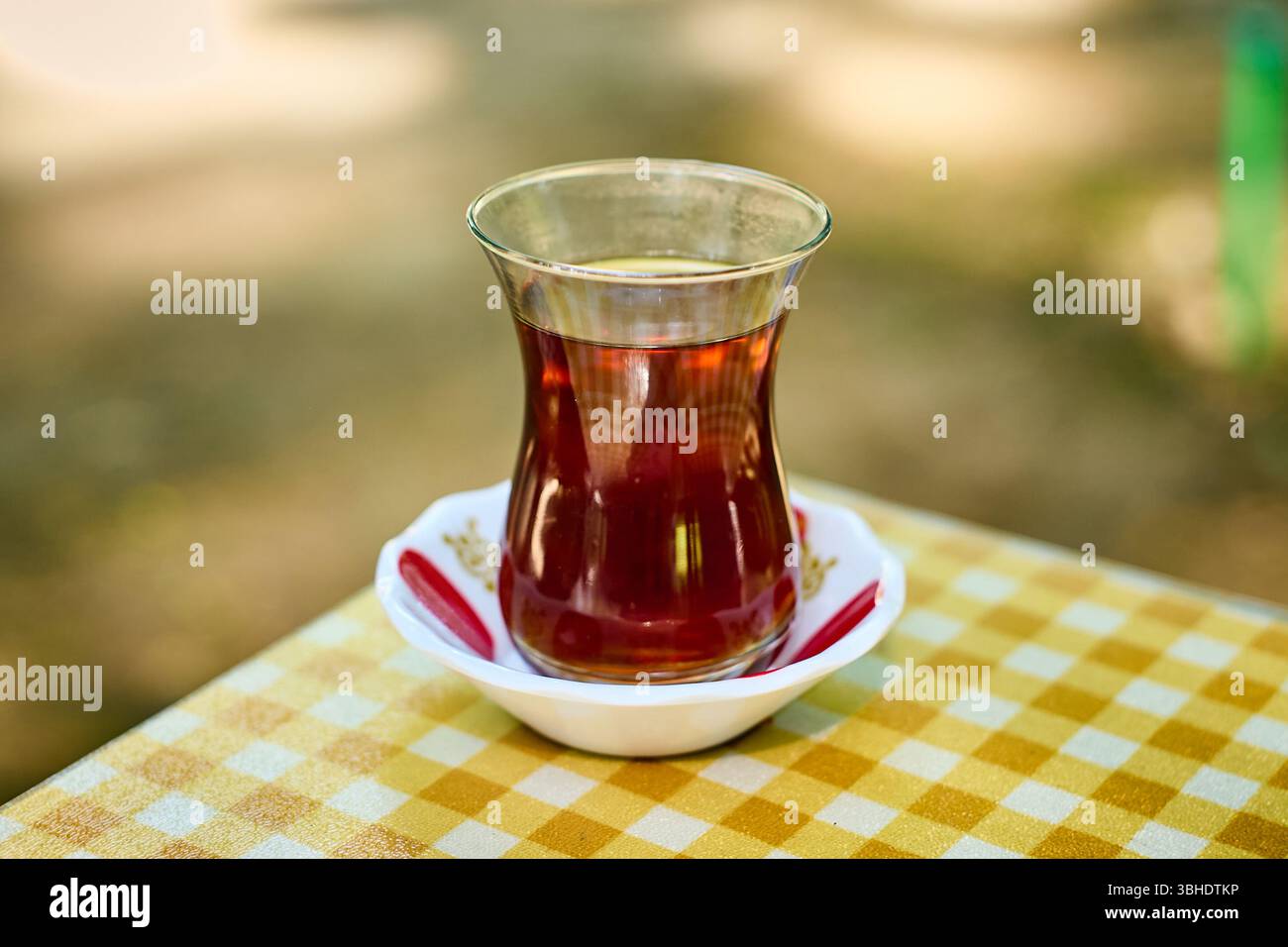 Un gros plan de thé noir aromatique dans un verre armudu classique, placé sur une nappe à carreaux brillante. Banque D'Images