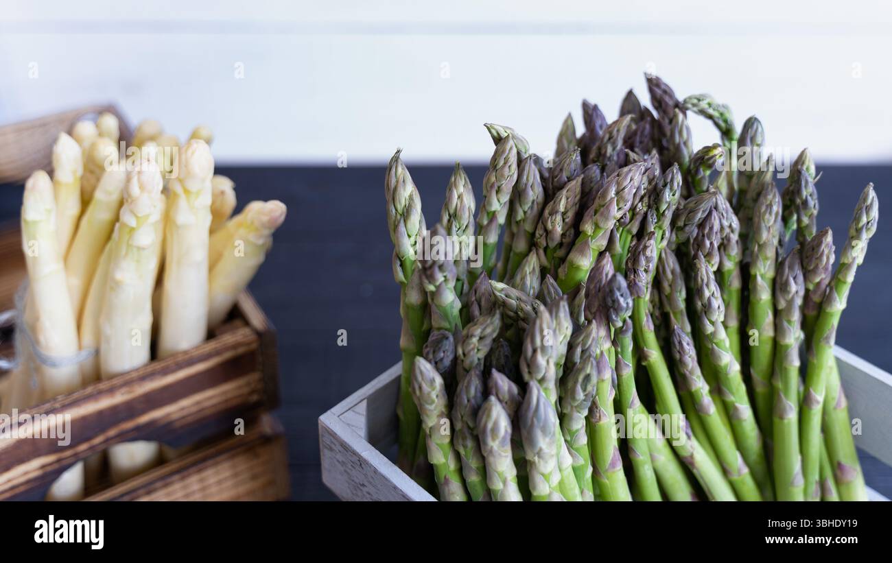 Un contraste visuel d'asperges vertes et blanches dans des caisses rustiques, idéal pour les thèmes de la récolte de printemps. Banque D'Images