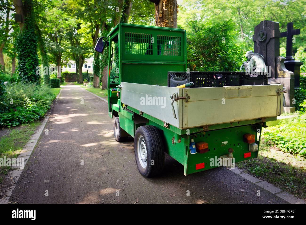 un petit camion électrique vert avec des jardinières sur la zone de chargement se trouve sur un chemin dans un cimetière Banque D'Images