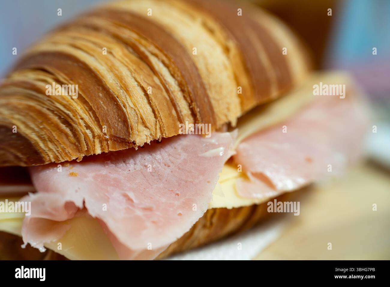 Un sandwich chaud et feuilleté de croissant rempli de jambon de première qualité et de fromage fondu, magnifiquement présenté sur une planche de bois. Parfait pour les menus de café, nourriture blo Banque D'Images