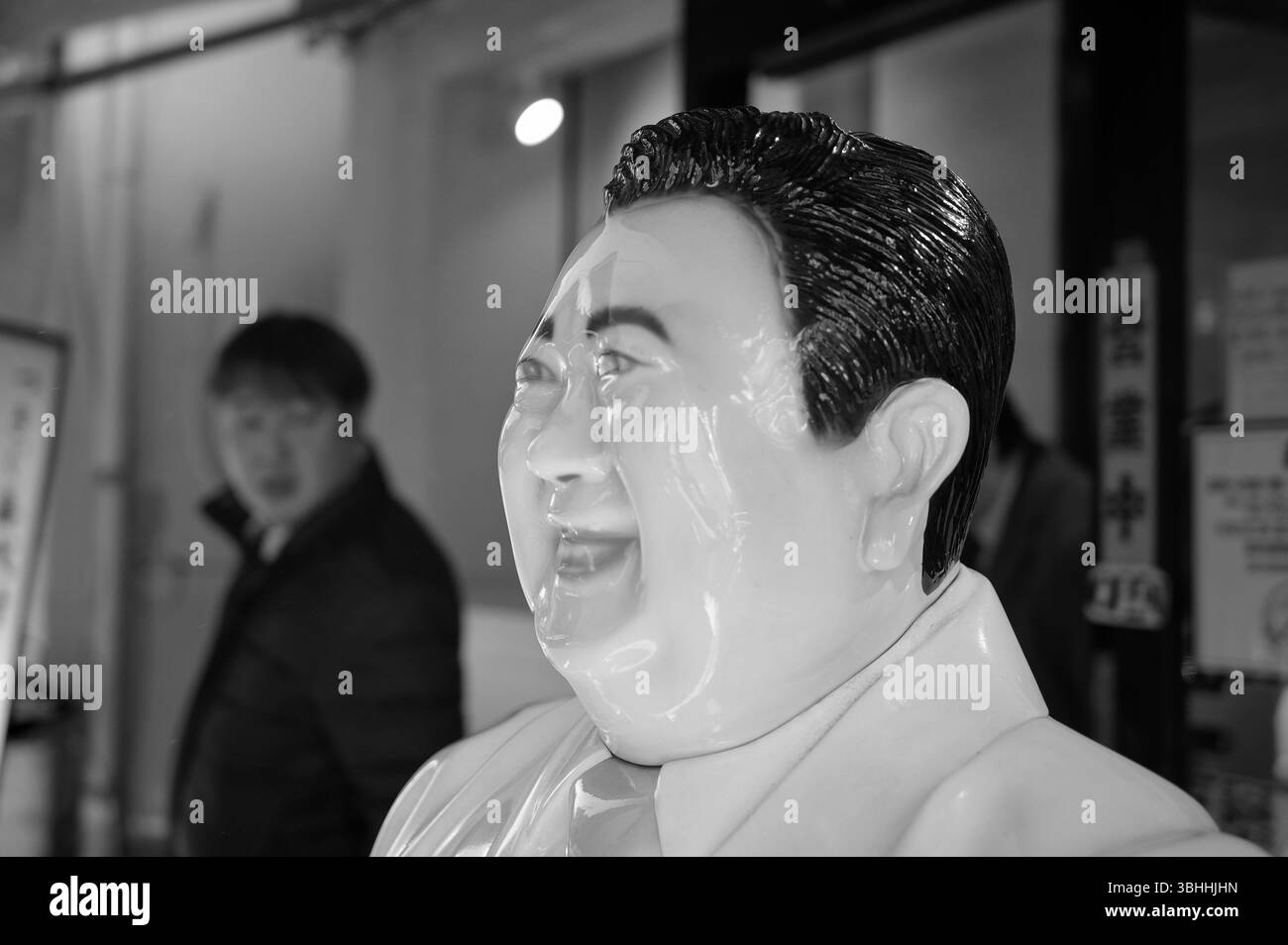 Statue brillante d'un homme souriant dans un costume, avec un passant qui la regarde en arrière-plan dans une rue de Tokyo Banque D'Images