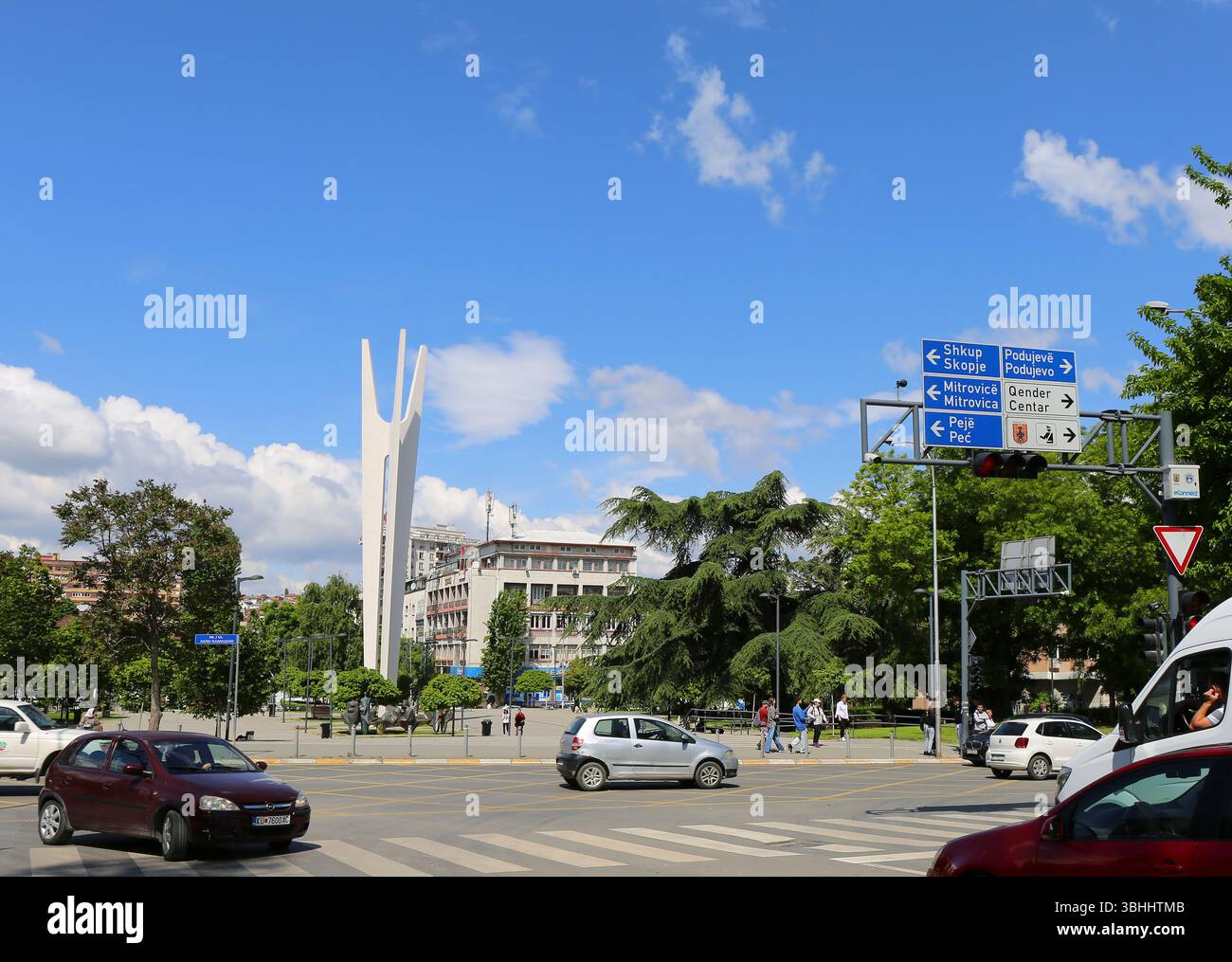 Rue avec des voitures, non identifiés marchant personnes, panneaux, panneaux de signalisation et Spomenik Monument à Pristina, Kosovo Banque D'Images