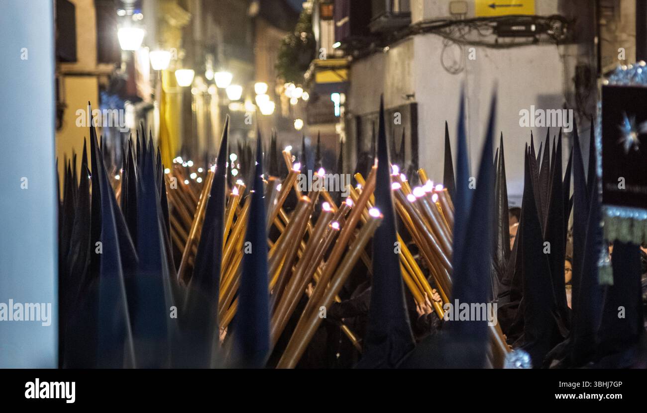 Nazarenos de Gran Poder défilent dans les rues de Séville tenant des bougies, créant une atmosphère solennelle pendant les festivités de la semaine Sainte. Banque D'Images