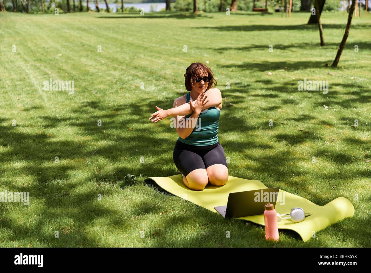 Fit et Pretty Woman s'étire tout en faisant de l'exercice à l'extérieur sur une zone herbeuse dans le parc, favorisant le fitness en ligne Banque D'Images