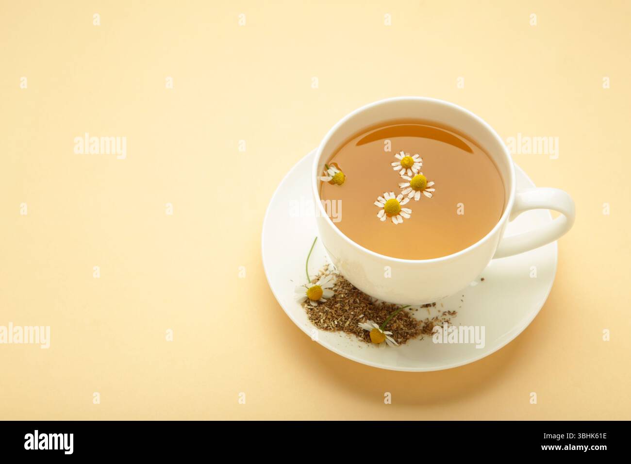 Tisane aromatique dans la tasse blanche et les camomilles sur fond beige. Vue de dessus Banque D'Images