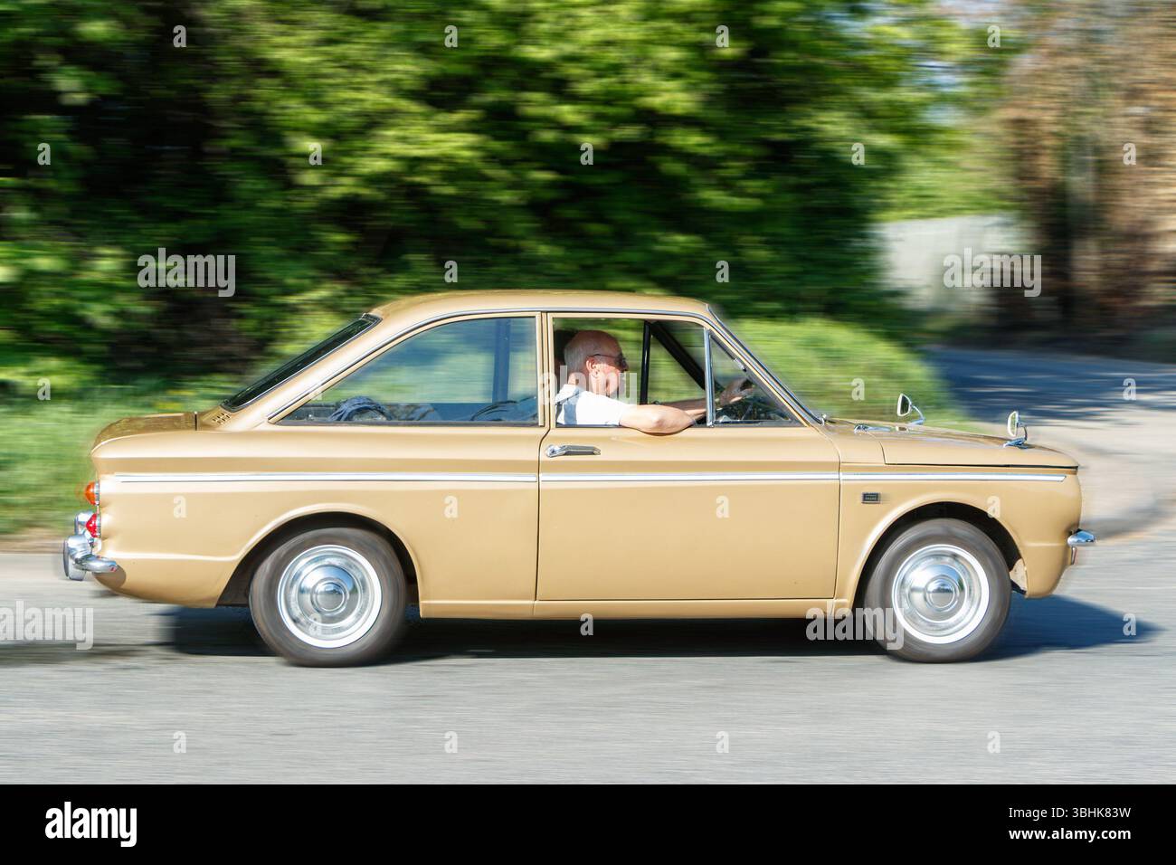 Voiture Hillman Imp brun vintage conduisant par une journée ensoleillée avec un fond flou de végétation verte et de route Banque D'Images